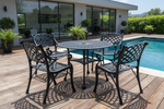 A 5-piece black metal patio bistro set including a round table and four matching armchairs, shown on a concrete patio with a garden background.